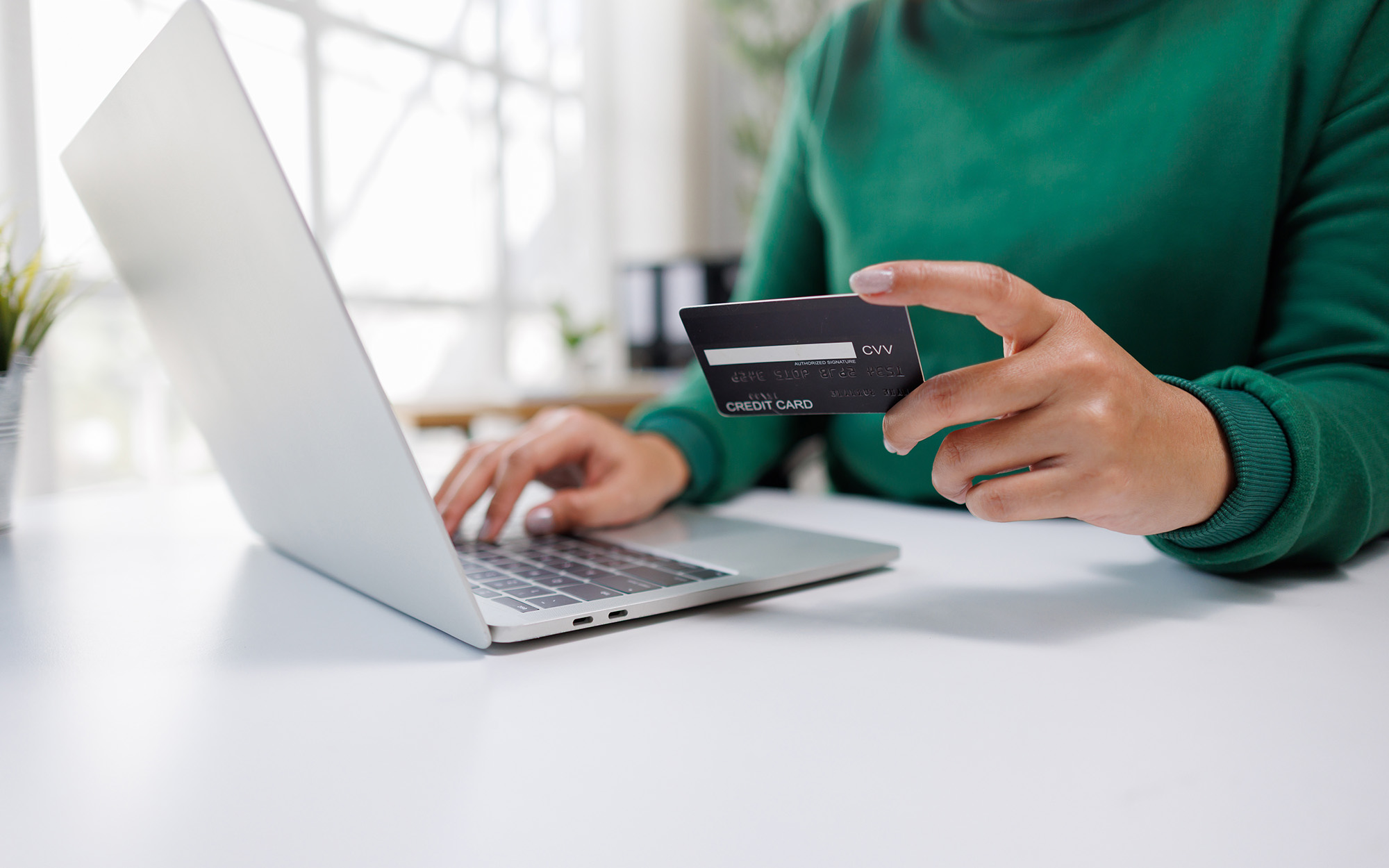 A person is engaged in online shopping, holding a credit card in one hand